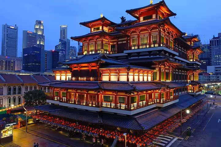 Illuminated Buddha Tooth Relic Temple glowing red at dusk in Singapore Chinatown with city skyline behind