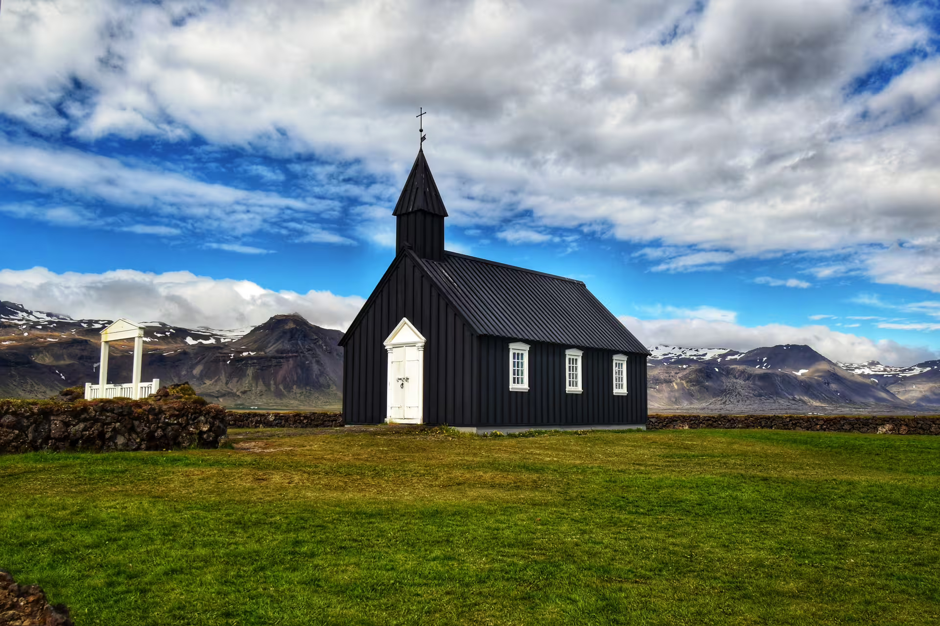 Black wooden church with white trim and steeple on Snaefellsnes Peninsula with snow-capped mountains behind