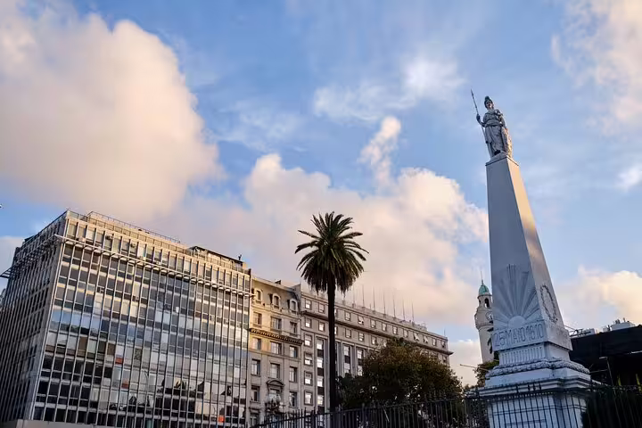 Pyramide de Mayo obelisk with statue atop in Plaza de Mayo, Buenos Aires, with palm tree and city buildings