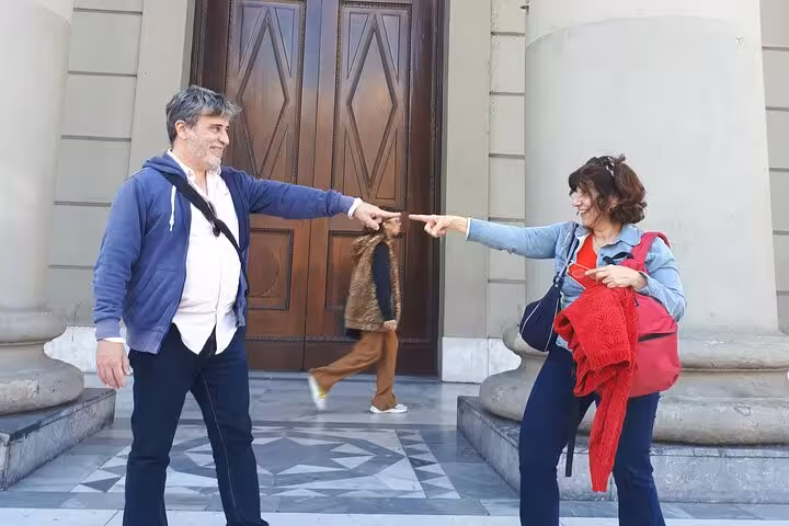 Two people pointing fingers at each other playfully in front of a historic building in Buenos Aires