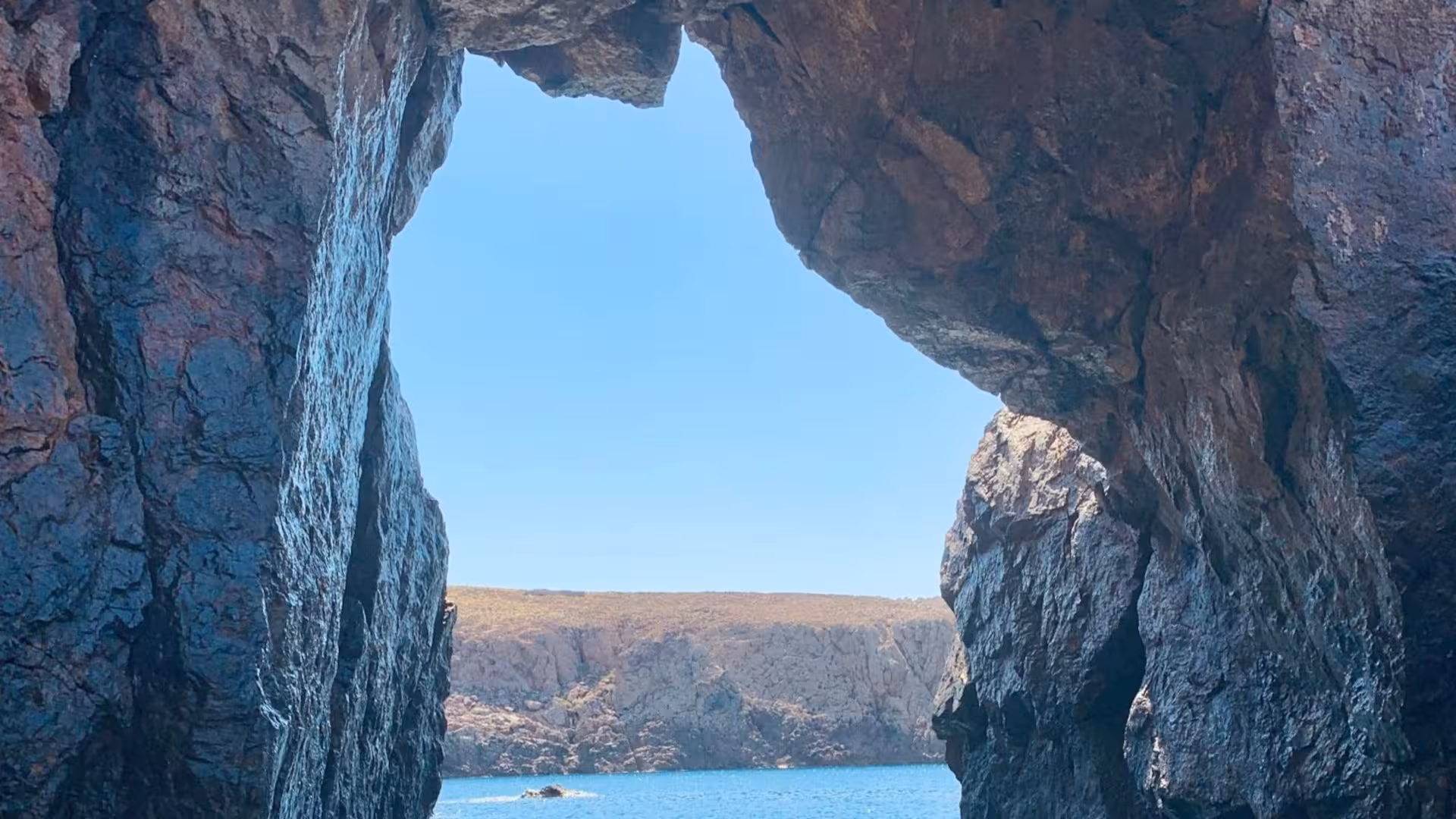 View through a rocky cave opening onto a serene sea in Buggerru, highlighting the natural beauty of the coastline.