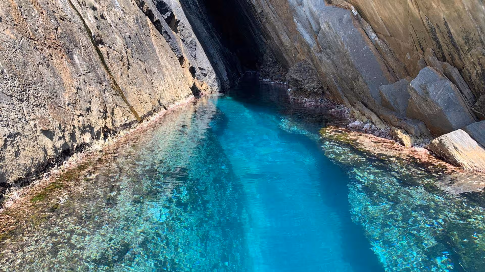 Crystal-clear turquoise waters leading into a narrow rock passage near Porto Flavia, perfect for exploration by dinghy.