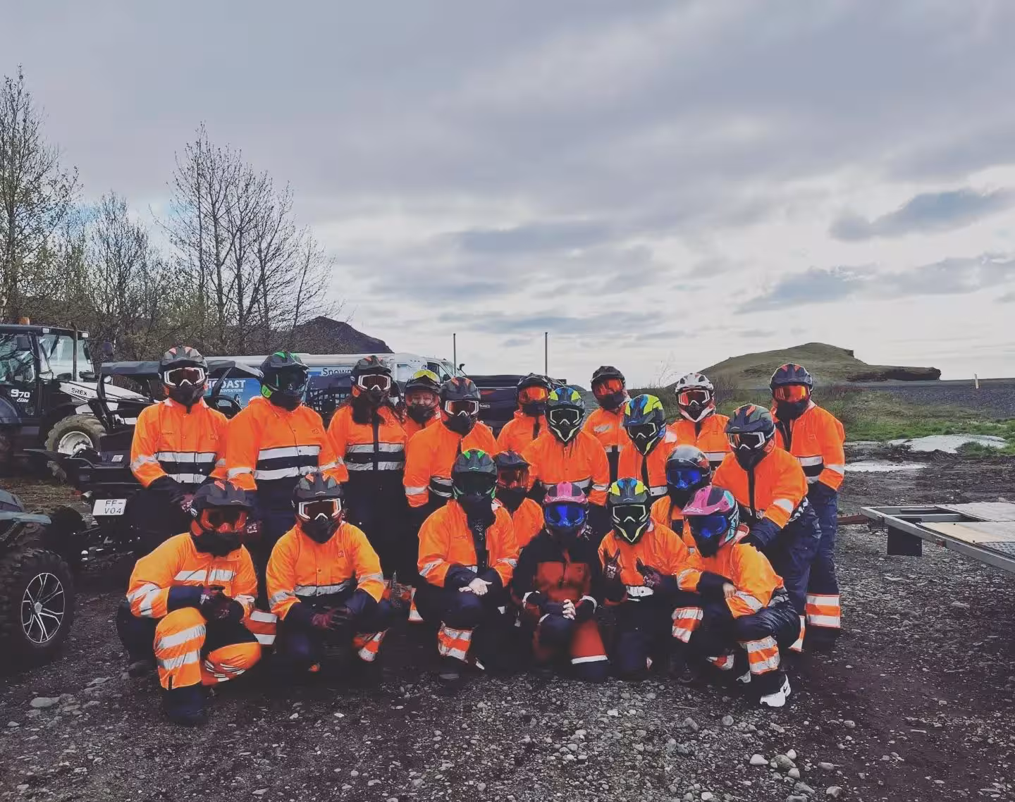 Group of buggy tour participants in orange safety suits and helmets posing in Iceland landscape