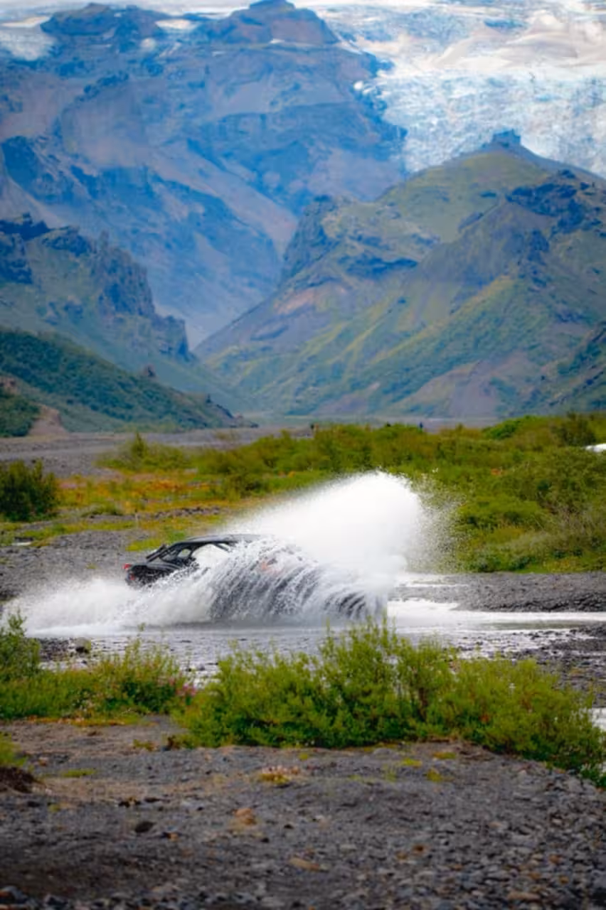 Black buggy ATV splashing through river crossing with glacier and green mountains in Iceland background