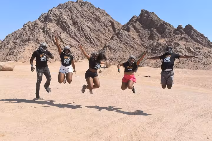 Group jumping in Sinai desert during Buggy Safari Sharm El Sheikh adventure with mountains and blue sky