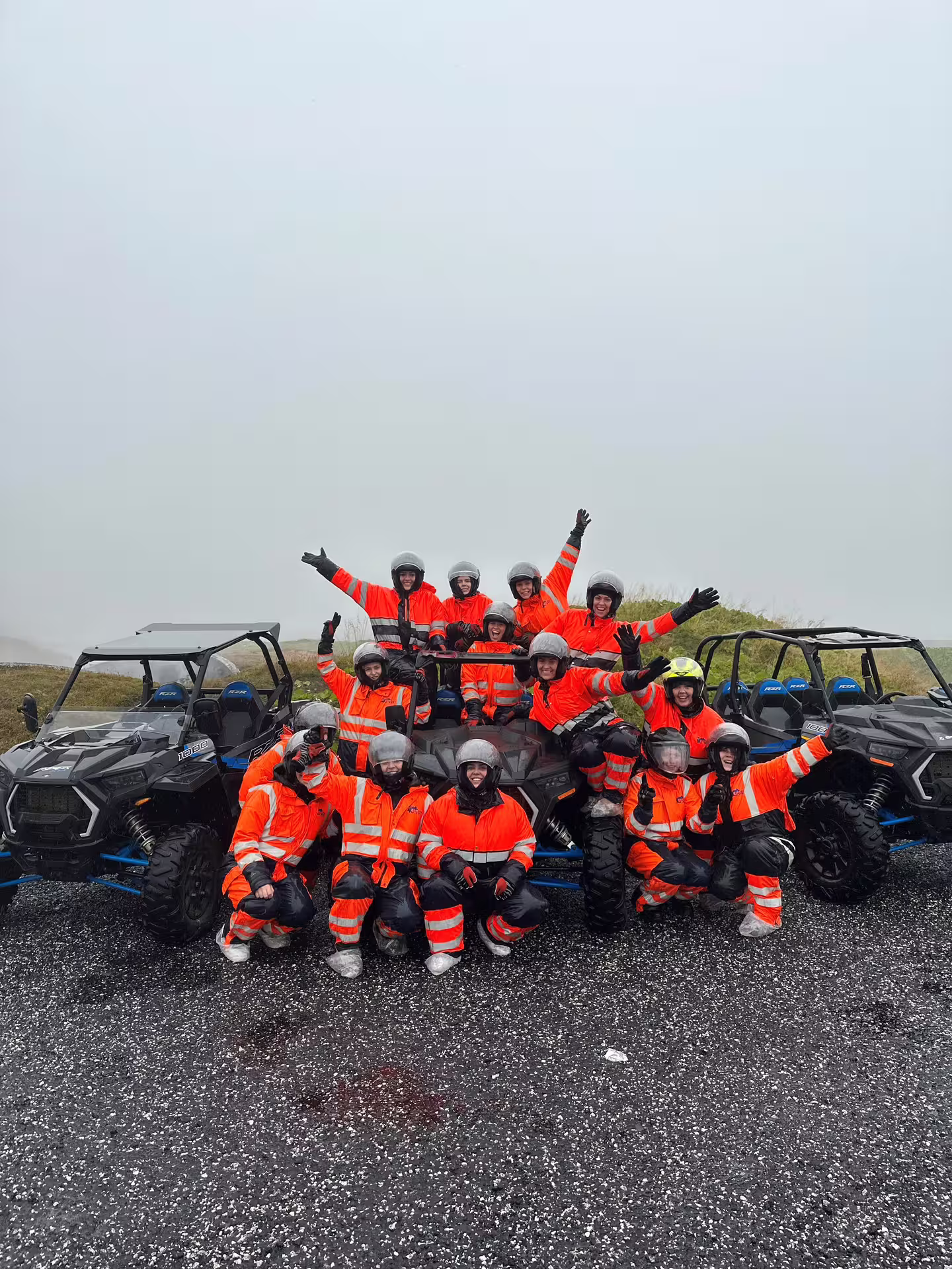 Group of tourists in orange safety suits and helmets posing with Polaris RZR buggies in Iceland
