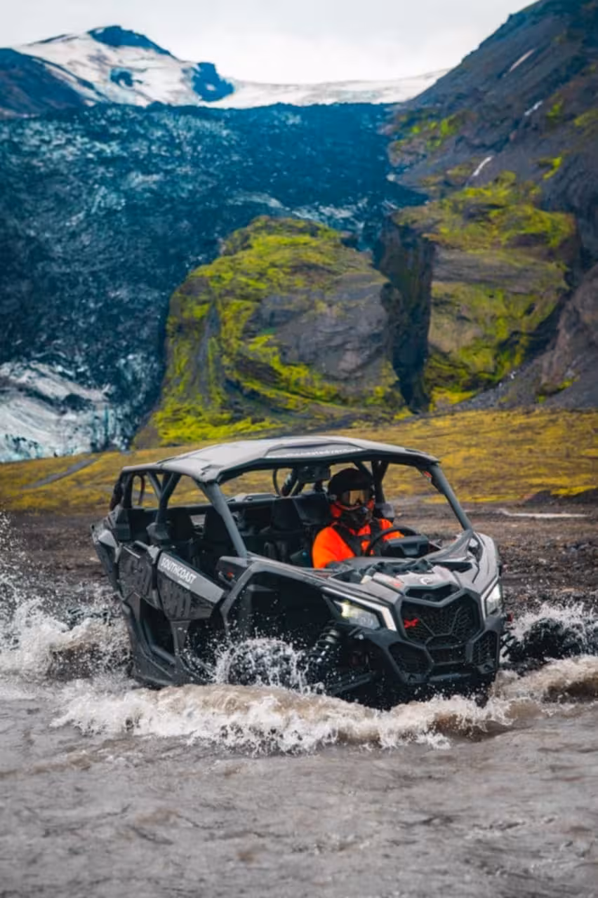 Off-road buggy splashing through glacial river with snow-capped Icelandic mountains in background