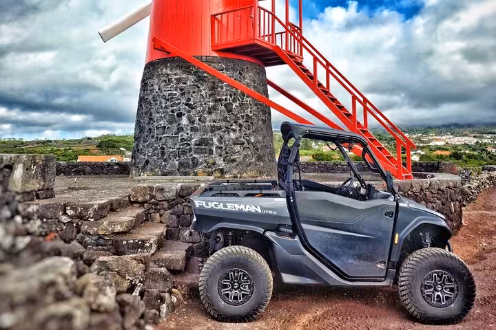 Buggy parked beside a traditional red windmill on Pico Island, highlighting scenic tour route.