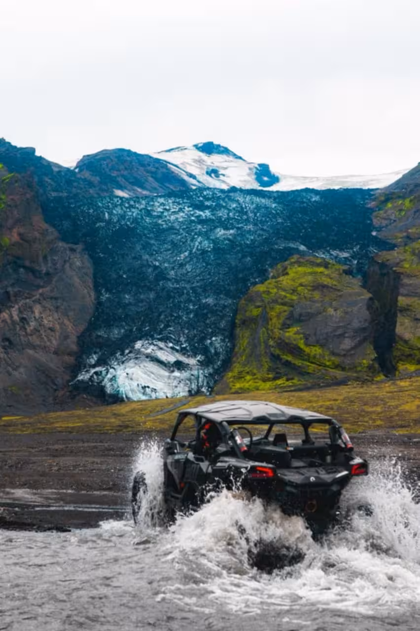 Black buggy UTV splashing through glacial river with Thorsmork glacier and green highlands in background