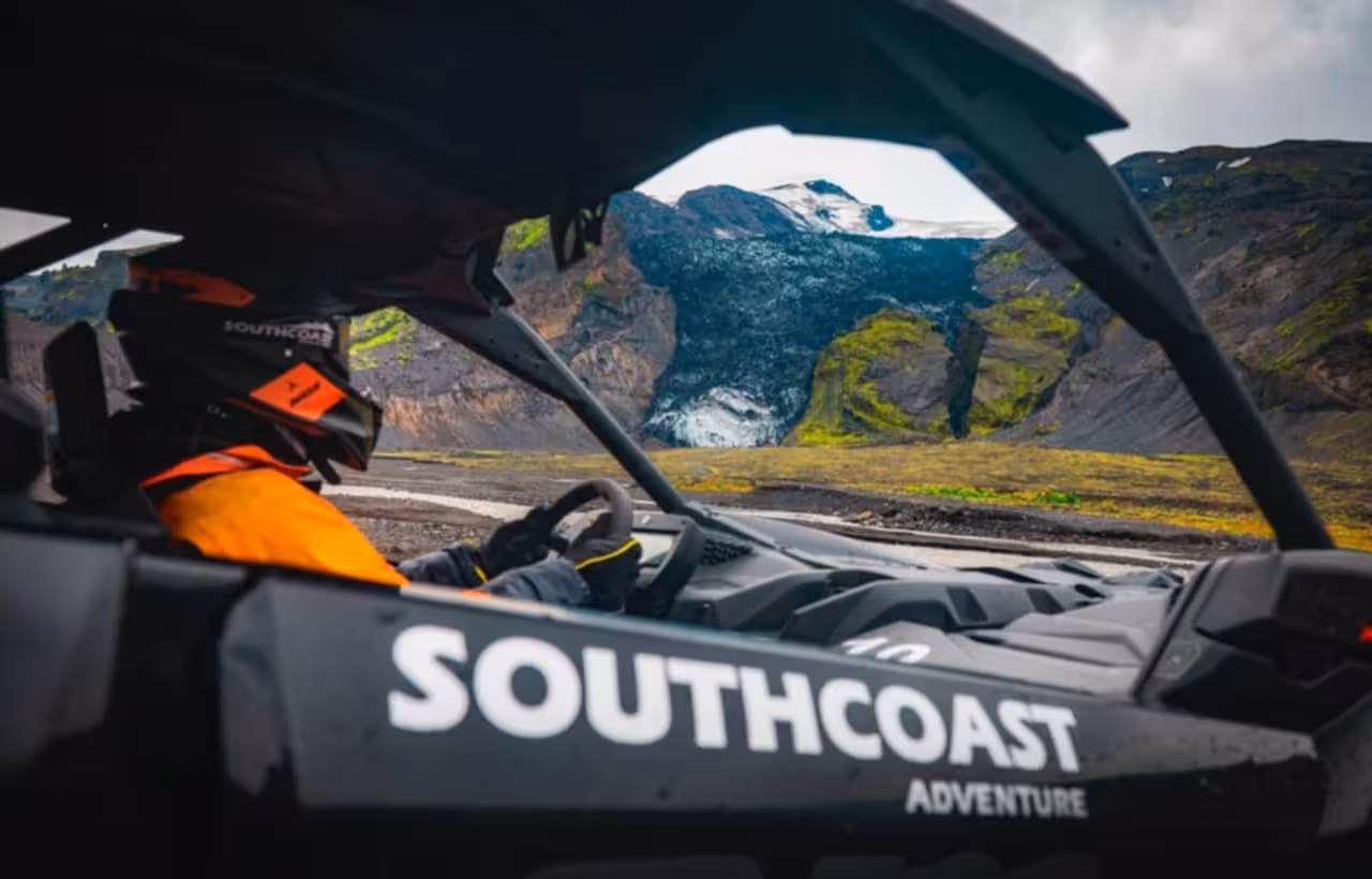 Driver in orange helmet navigating Southcoast Adventure buggy through volcanic Thorsmork landscape with glacier backdrop