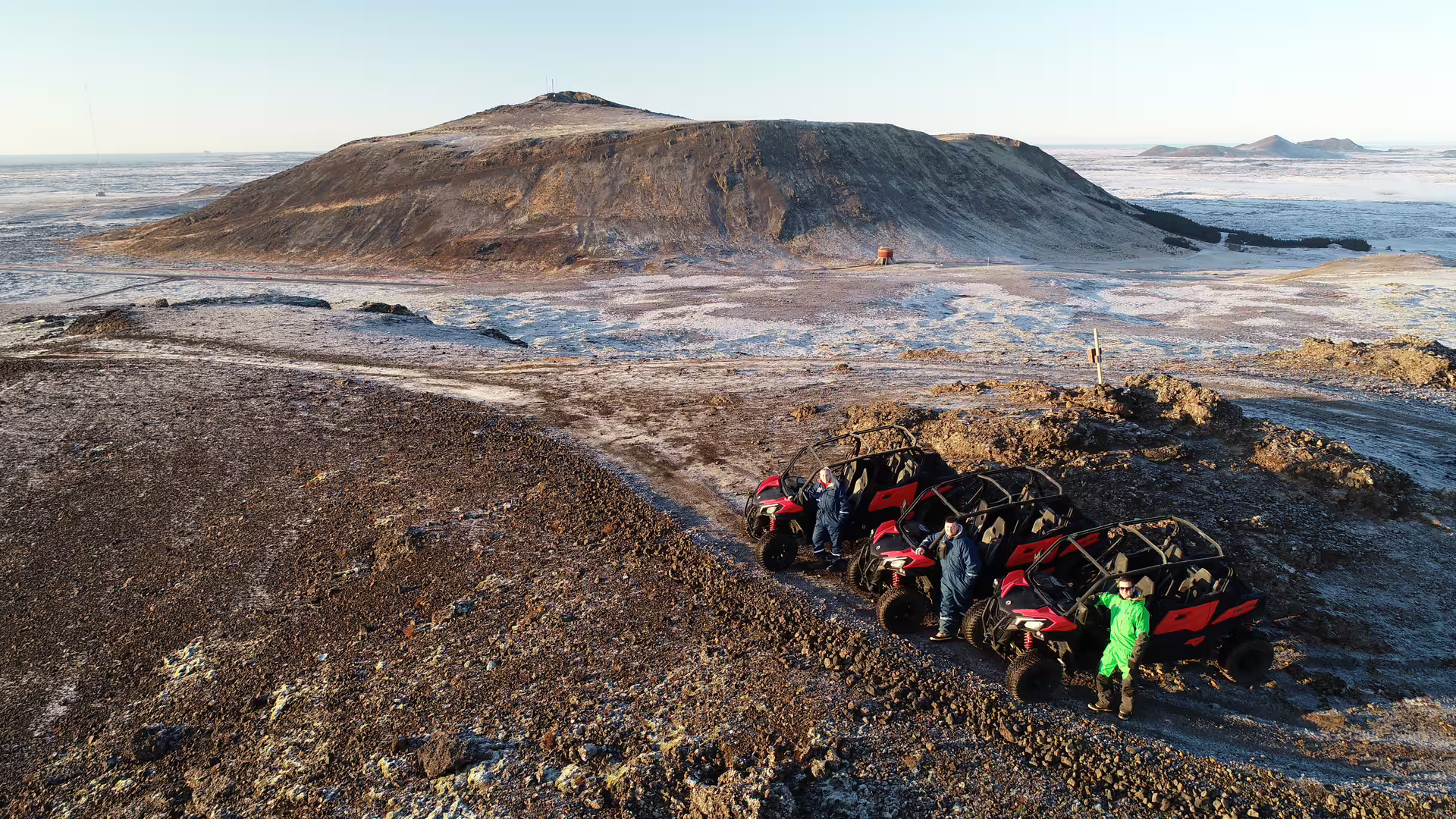 Red buggy UTVs parked on volcanic lava fields with a crater hill in the background in Iceland