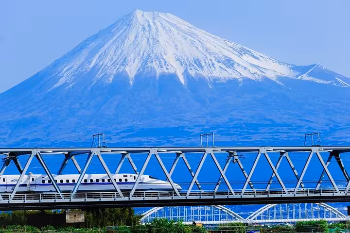 Bullet train crossing a bridge with majestic Mount Fuji in the background, highlighting the tour's convenience.
