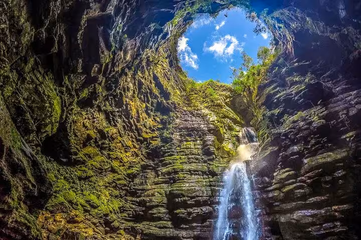 Stunning view of Buraco do Padre's waterfall cascading into a cavern illuminated by sunlight from above.