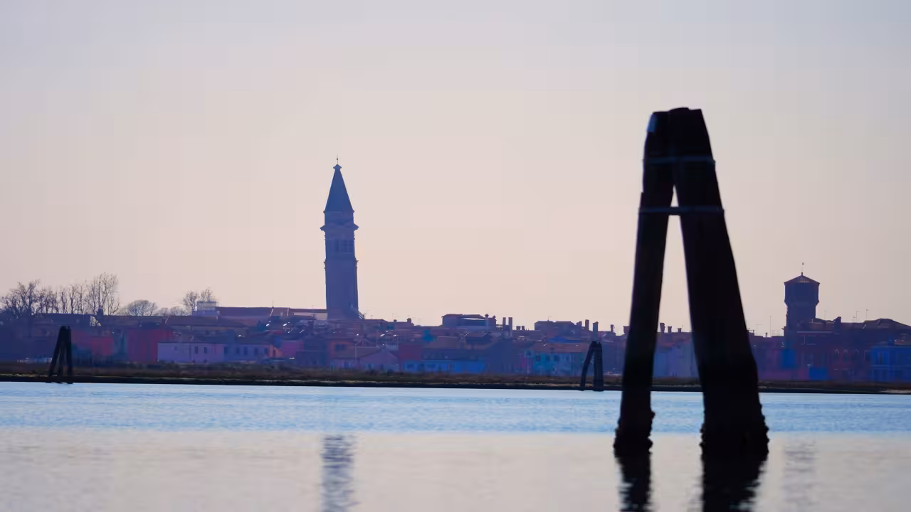 Silhouette of Burano bell tower across Venice lagoon at sunset, scenic view on Burano & Mazzorbo day trip