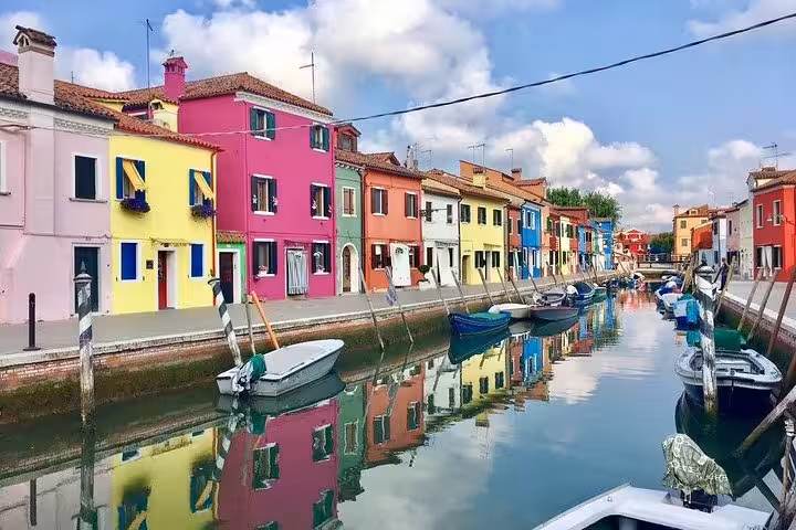 Colorful houses along Burano canal with boats, showcasing vibrant Venetian charm on a luxury day tour.