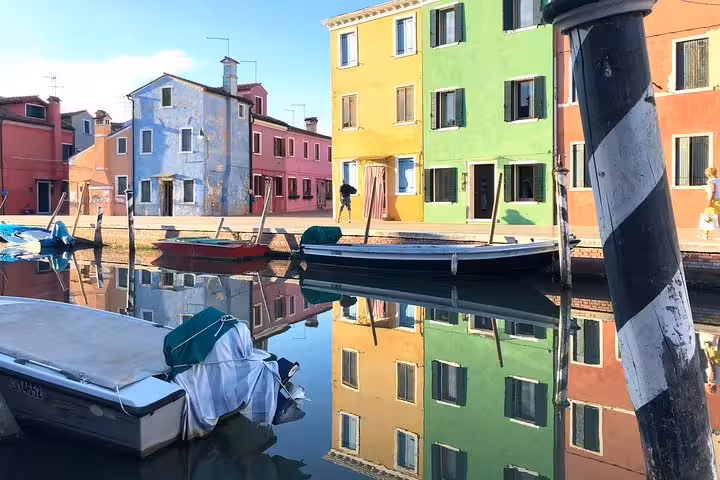 Brightly colored houses reflecting in the canal waters of Burano, featured in the Murano and Burano shared tour.