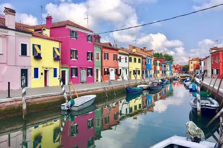 Colorful houses lining the canal in Burano, reflecting in the water, perfect for a scenic boat tour through Venice.