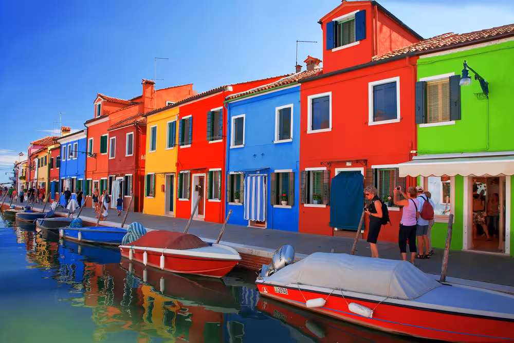 Vibrant Burano houses reflecting in the canal, showcasing the colorful charm of Venice Islands tours.