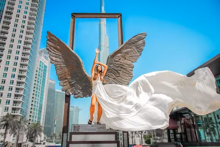 Elegant woman in a white dress with angel wings frames the Burj Khalifa in this captivating Dubai videography session.