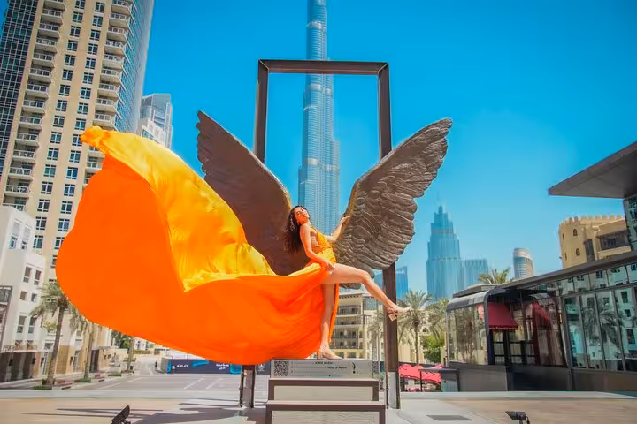Woman in a flowing orange dress with angel wings in front of Burj Khalifa, ideal for Instagram videography.