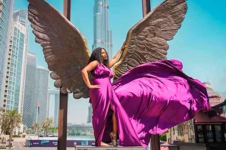 Elegant woman in a flowing purple dress poses with angel wings, Burj Khalifa soaring in the background, Dubai videography shoot.