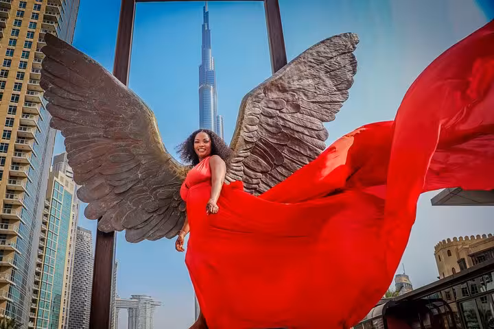 Woman in a dramatic red dress with angel wings, set against the iconic Burj Khalifa, creating a striking Instagram shot.