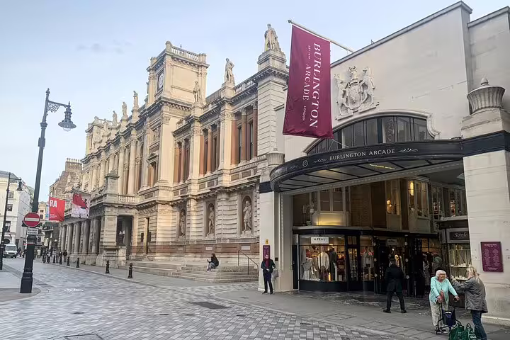 Burlington Arcade entrance on Piccadilly, London, with ornate neoclassical facade and shoppers on the pavement