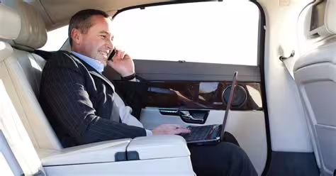 Business traveler working on laptop in luxury private car during transfer from Naples to Paestum with professional driver