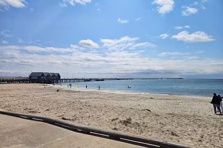 Scenic view of Busselton Jetty extending into the ocean under a bright blue sky with people enjoying the sandy beach.