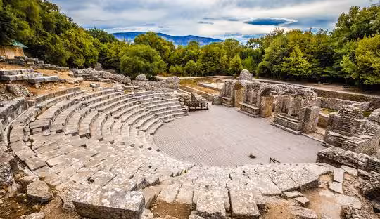 Ancient stone amphitheater of Butrint, Albania, nestled amidst lush greenery and showcasing historical architecture.