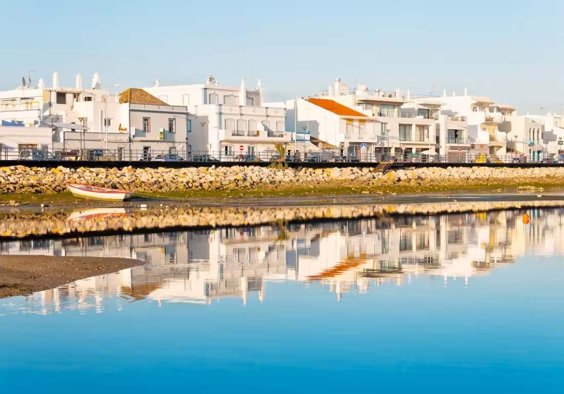Scenic waterfront view of Cabanas de Tavira with white buildings beautifully reflected in the calm blue lagoon waters