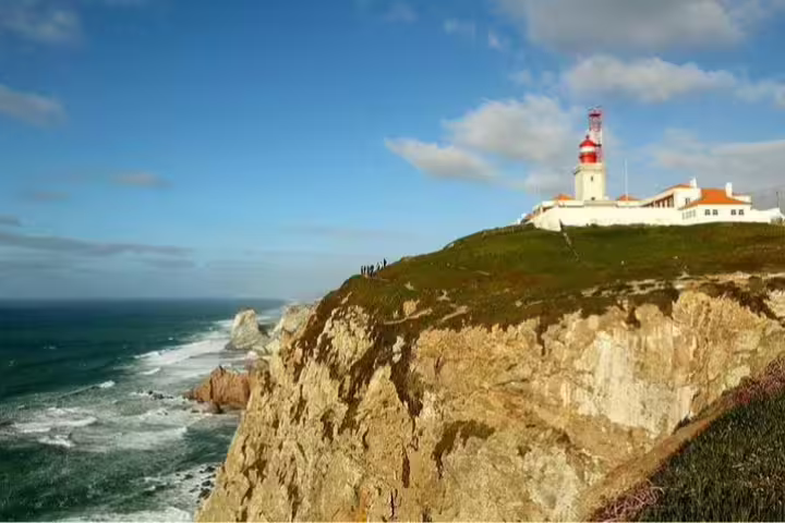 Scenic view of Cabo da Roca lighthouse perched on rugged cliffs with ocean backdrop, part of Sintra-Cascais panoramic tour.