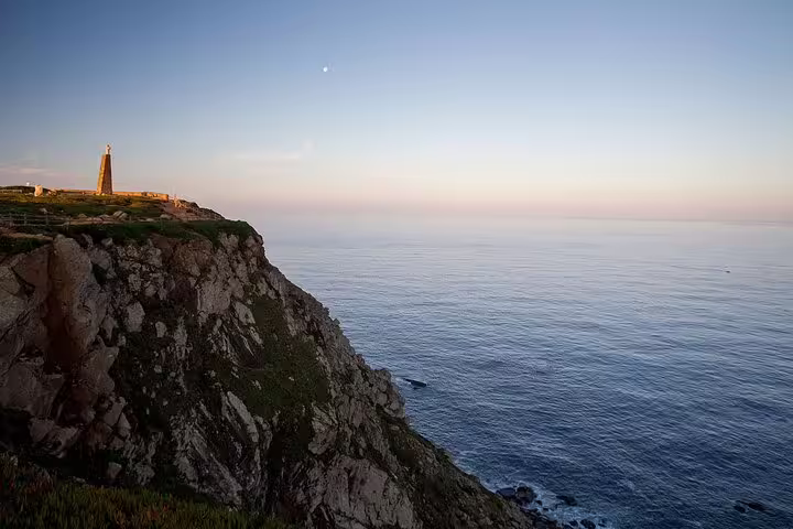 Sunset view of Cabo da Roca's rocky cliffs meeting the Atlantic Ocean with a distant lighthouse.