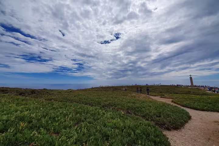 Visitors explore lush greenery and dramatic skies at Cabo da Roca during a private full-day tour from Lisbon, Portugal.