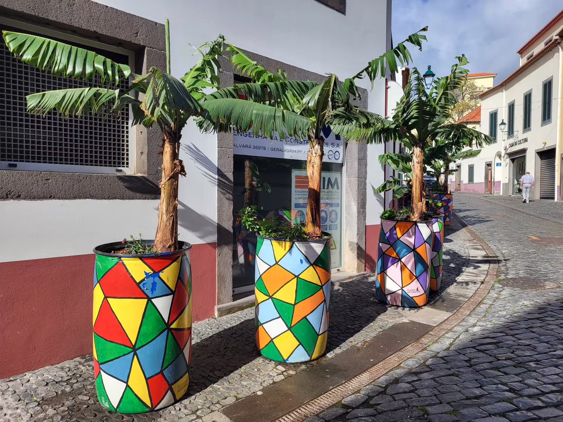 Colorful geometric planters line a cobblestone street in Madeira, showcasing local art and charm on the Cabo Girão tour.