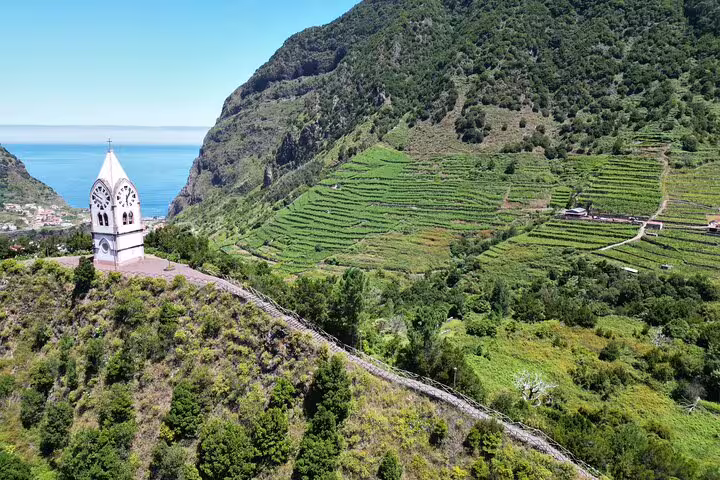 Aerial view of Cabo Girão sea cliffs with lush vineyards and a scenic church tower, perfect for a 4x4 wine tour adventure.