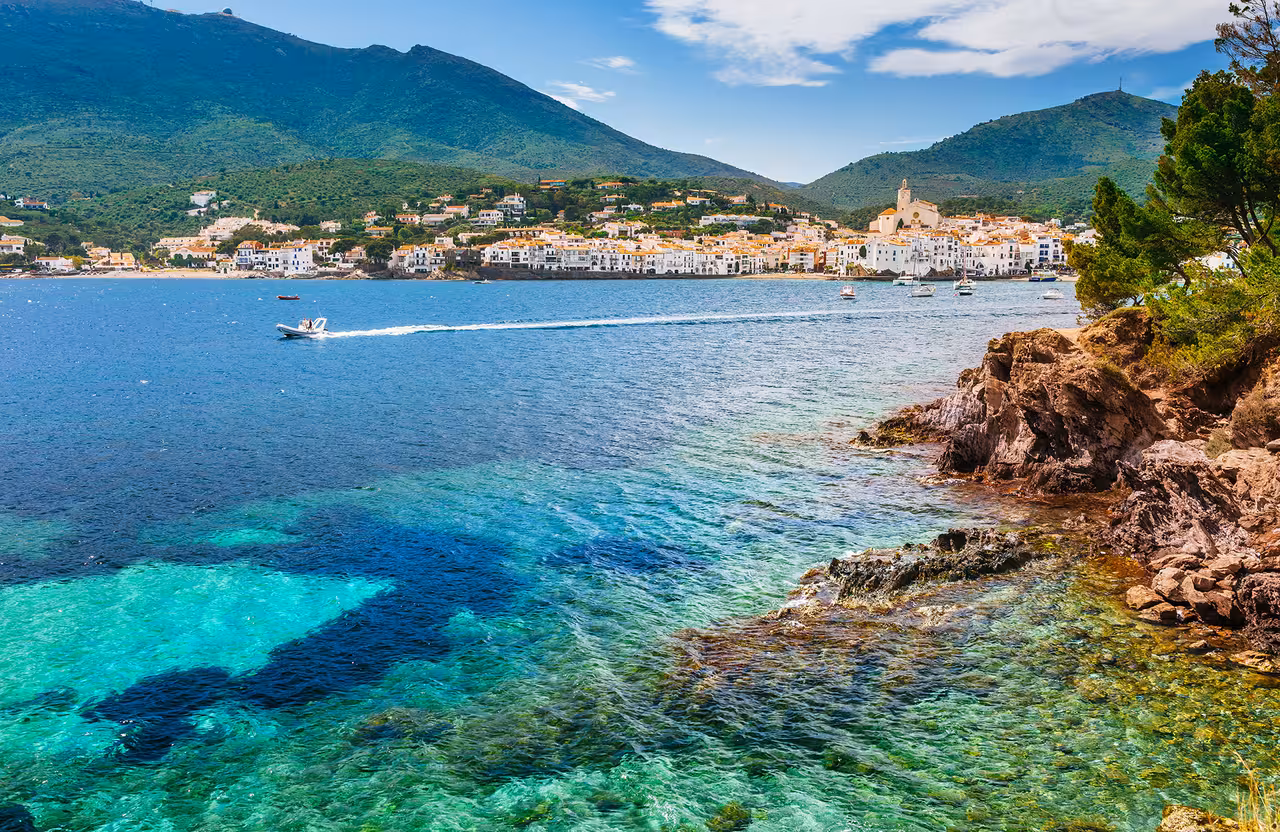 Scenic view of Cadaqués coastline with vibrant turquoise waters and lush green hills.