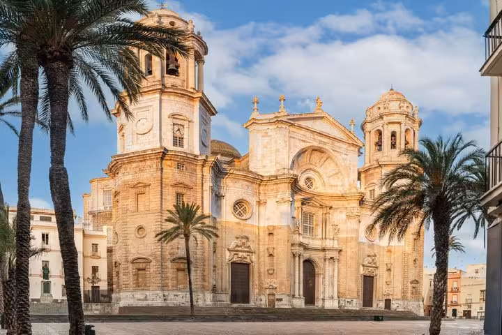 Baroque facade of Cadiz Cathedral with twin bell towers and palm trees in plaza