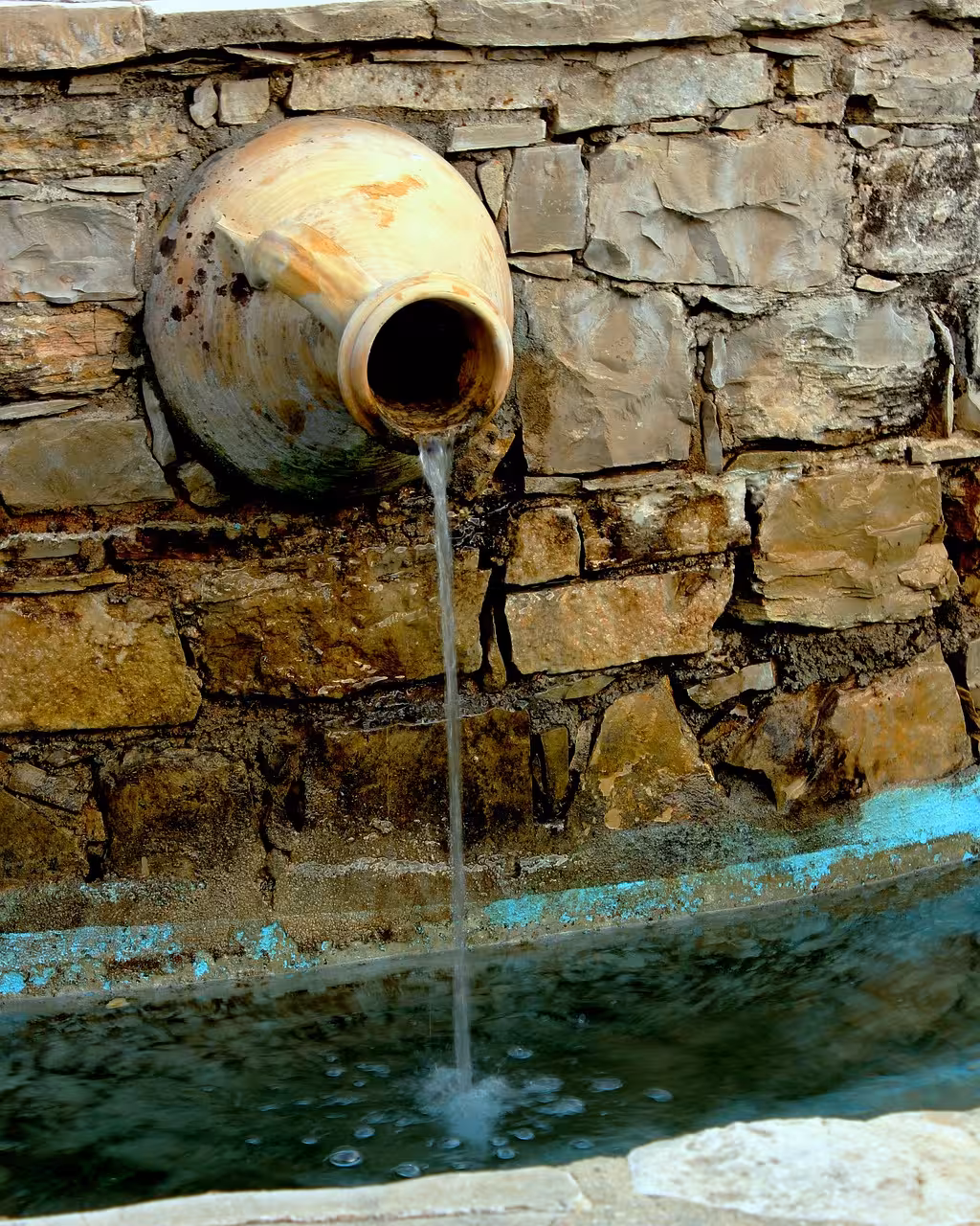 Rustic stone wall with flowing water from a traditional clay jug in Cadiz, Spain, highlighting local heritage.