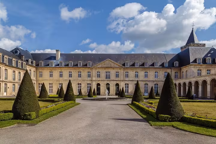 Grand courtyard of a historic French château in Caen with cone-shaped topiary trees and central fountain