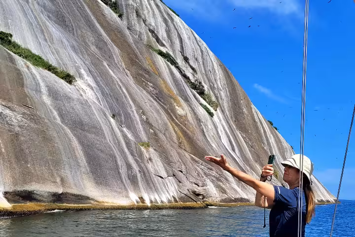 Tourist photographing Cagarras Archipelago's rugged cliffs from a boat, highlighting adventure and breathtaking ocean scenery.