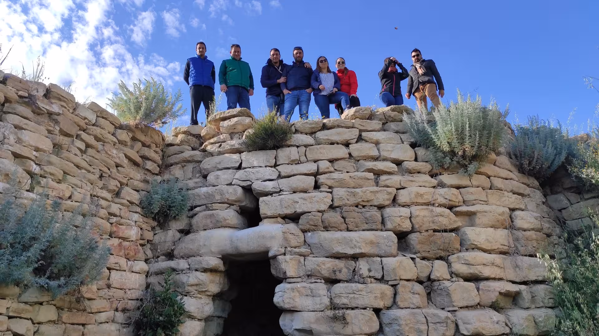 Group exploring ancient stone ruins on the Cagliari ATV tour from Guasila, under a clear blue sky.