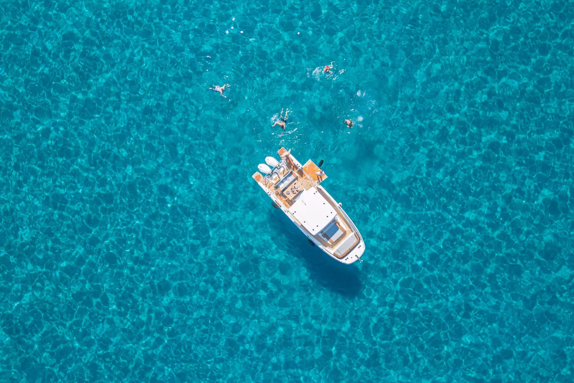 Aerial view of a boat surrounded by swimmers in crystal-clear waters on a Cagliari 3-hour boat tour.