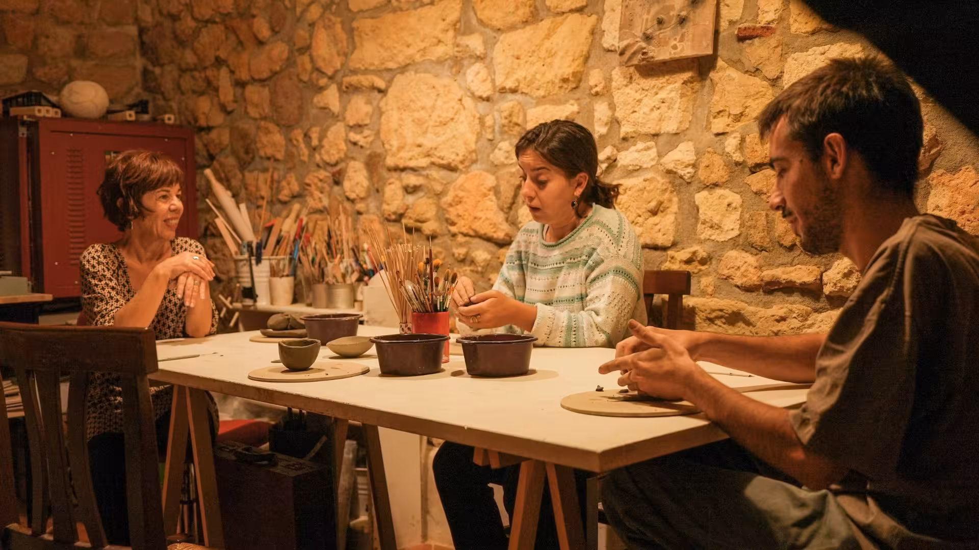 Three people engaged in a ceramics workshop in Cagliari, working on pottery in a cozy, rustic setting.