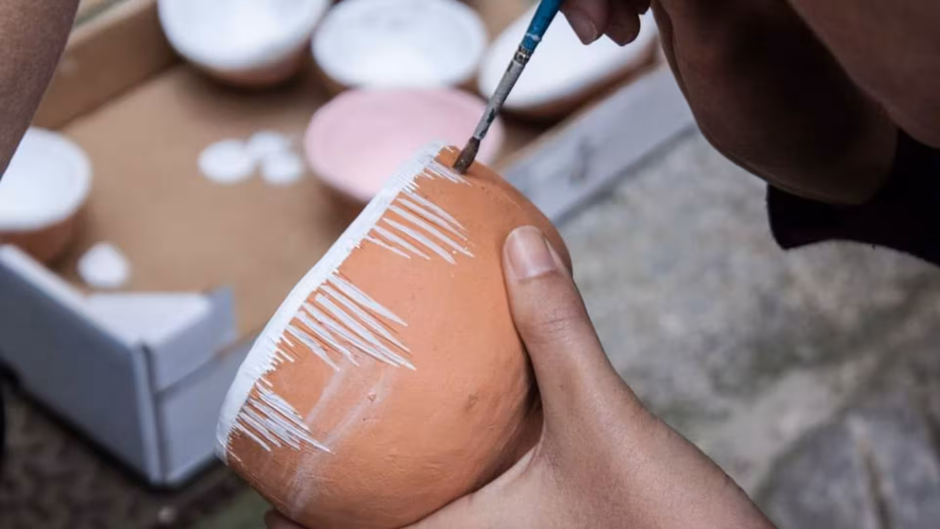 Close-up of hands painting a terracotta pot with white patterns in a Cagliari ceramics workshop.