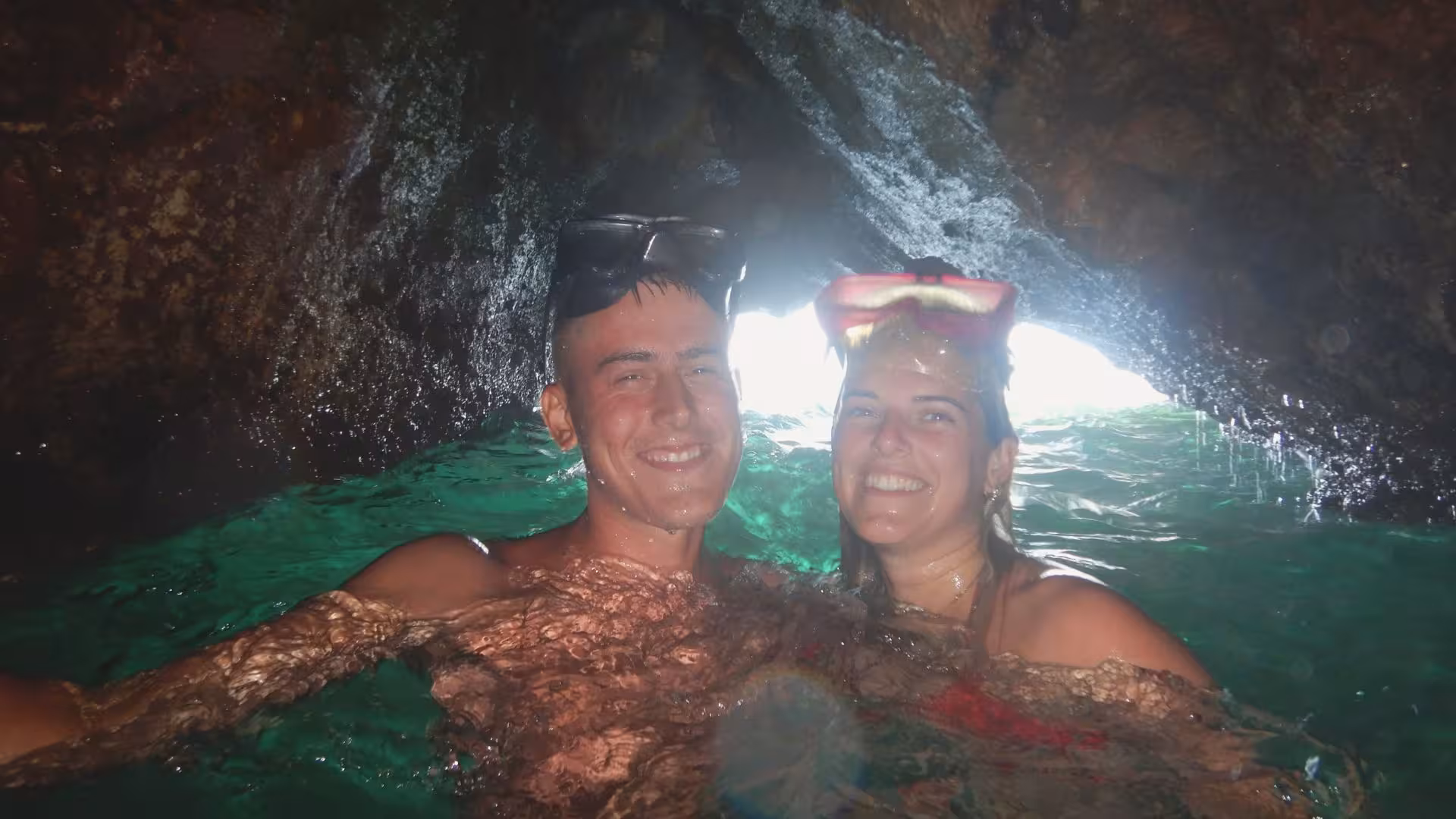 Couple snorkeling in a sunlit cave in Cagliari, smiling and enjoying the clear blue waters of the Mediterranean.