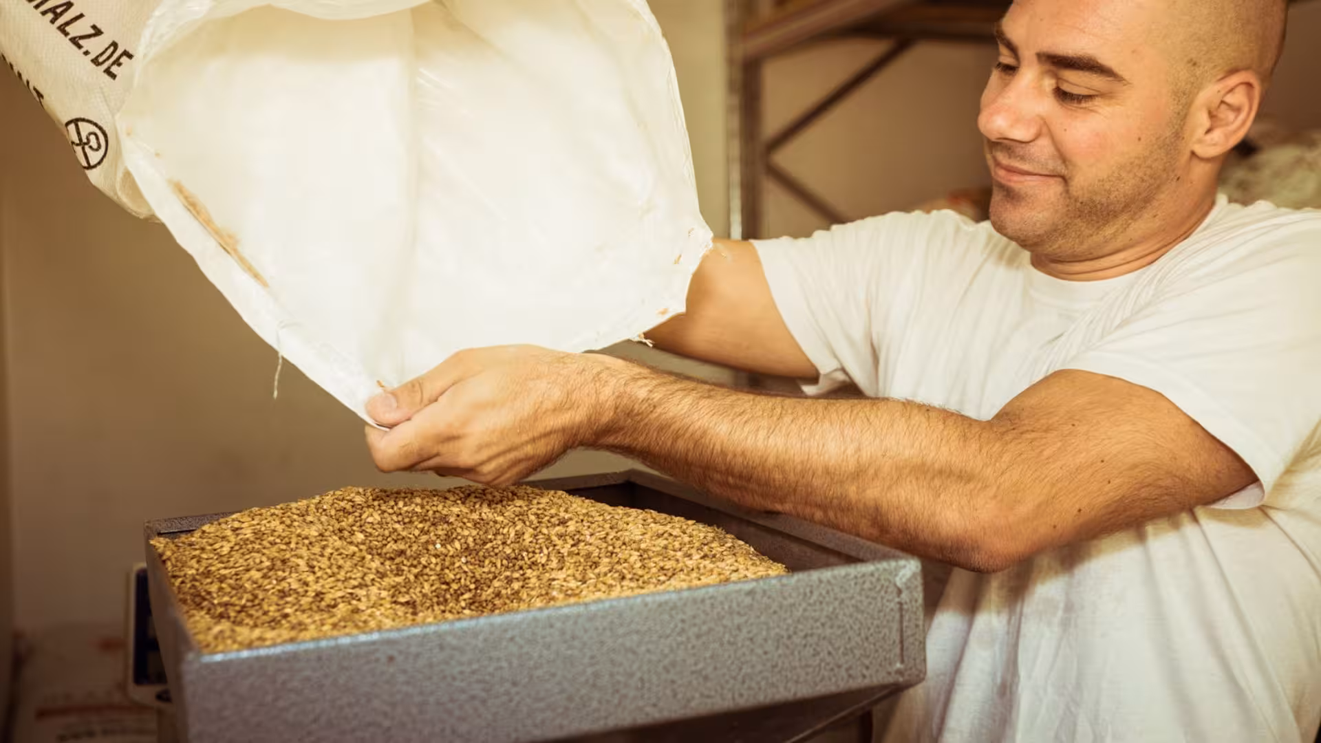 Brewer pouring grains into a grinder at a Cagliari craft brewery, highlighting the start of the beer brewing process.