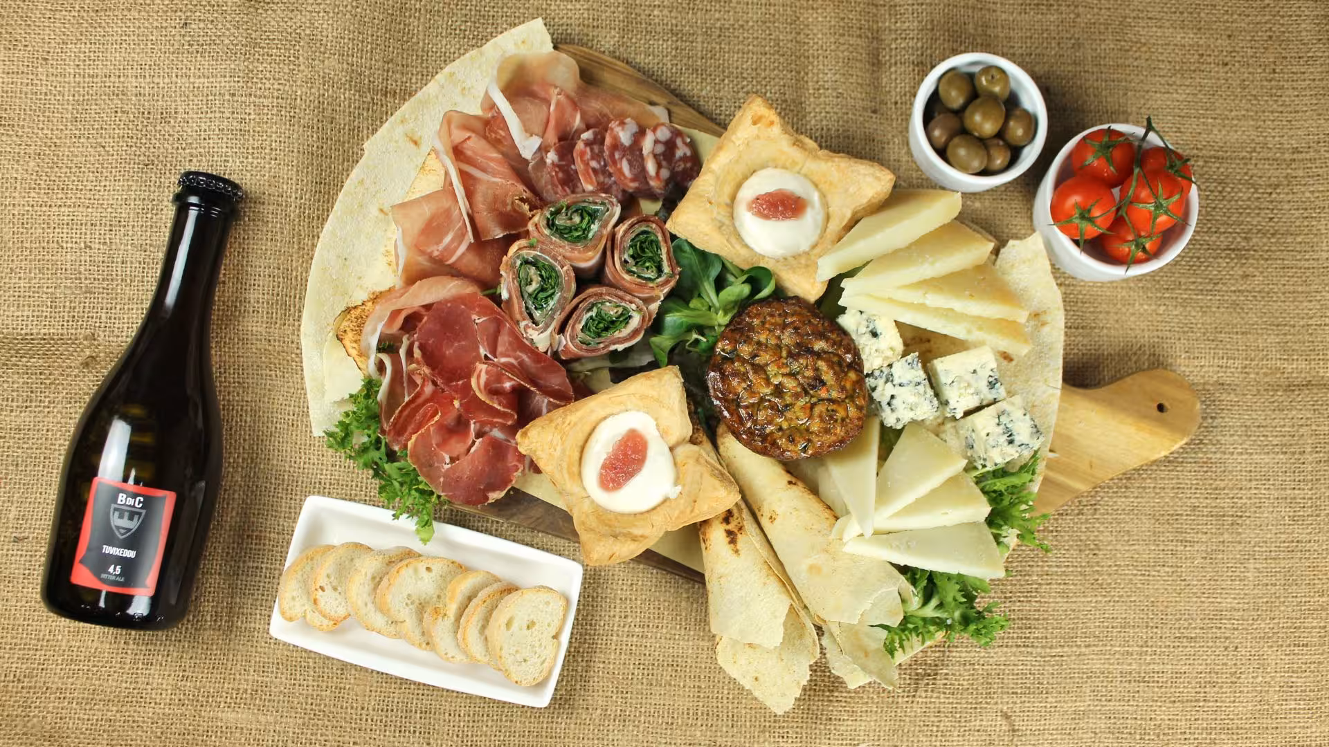 Charcuterie platter with Italian meats, cheeses, and a craft beer bottle on a rustic burlap background in Cagliari.