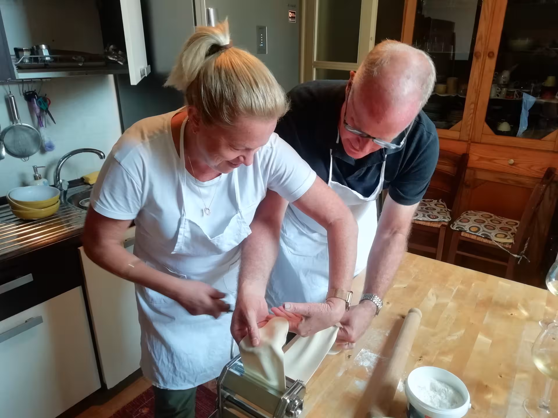 Two people joyfully using a pasta machine in a Cagliari culurgiones cooking class, highlighting hands-on learning.