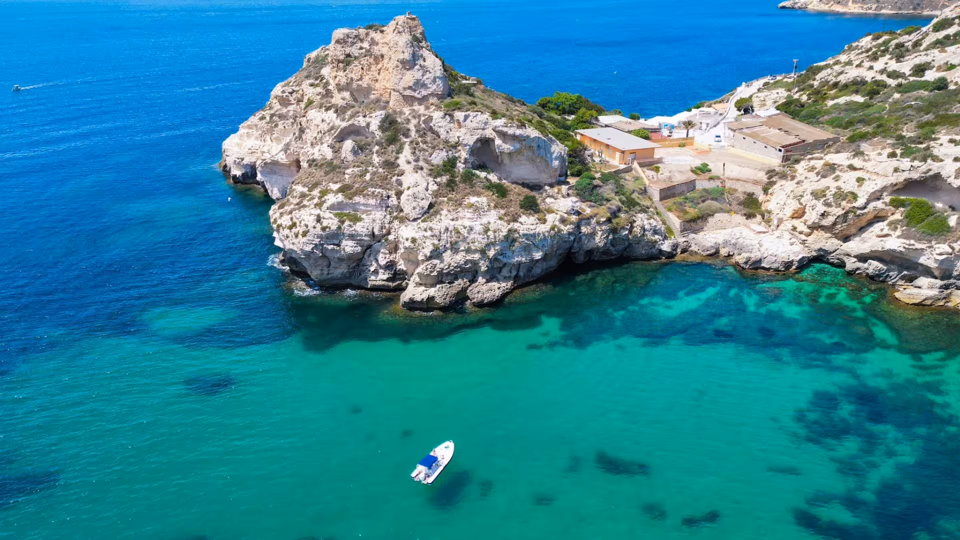 Aerial view of a dinghy floating near rugged Cagliari coastline with clear turquoise waters, ideal for scenic tours.